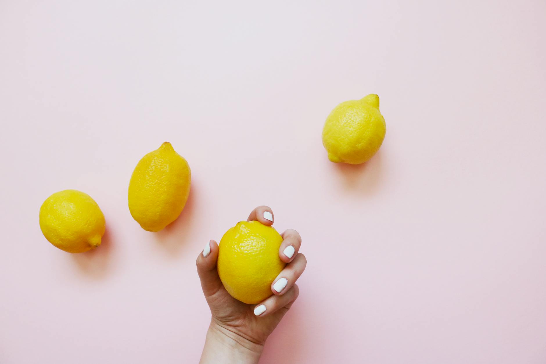 Une main tenant un citron frais sur fond rose poudré, symbole de la sensibilité cyclique du plaisir