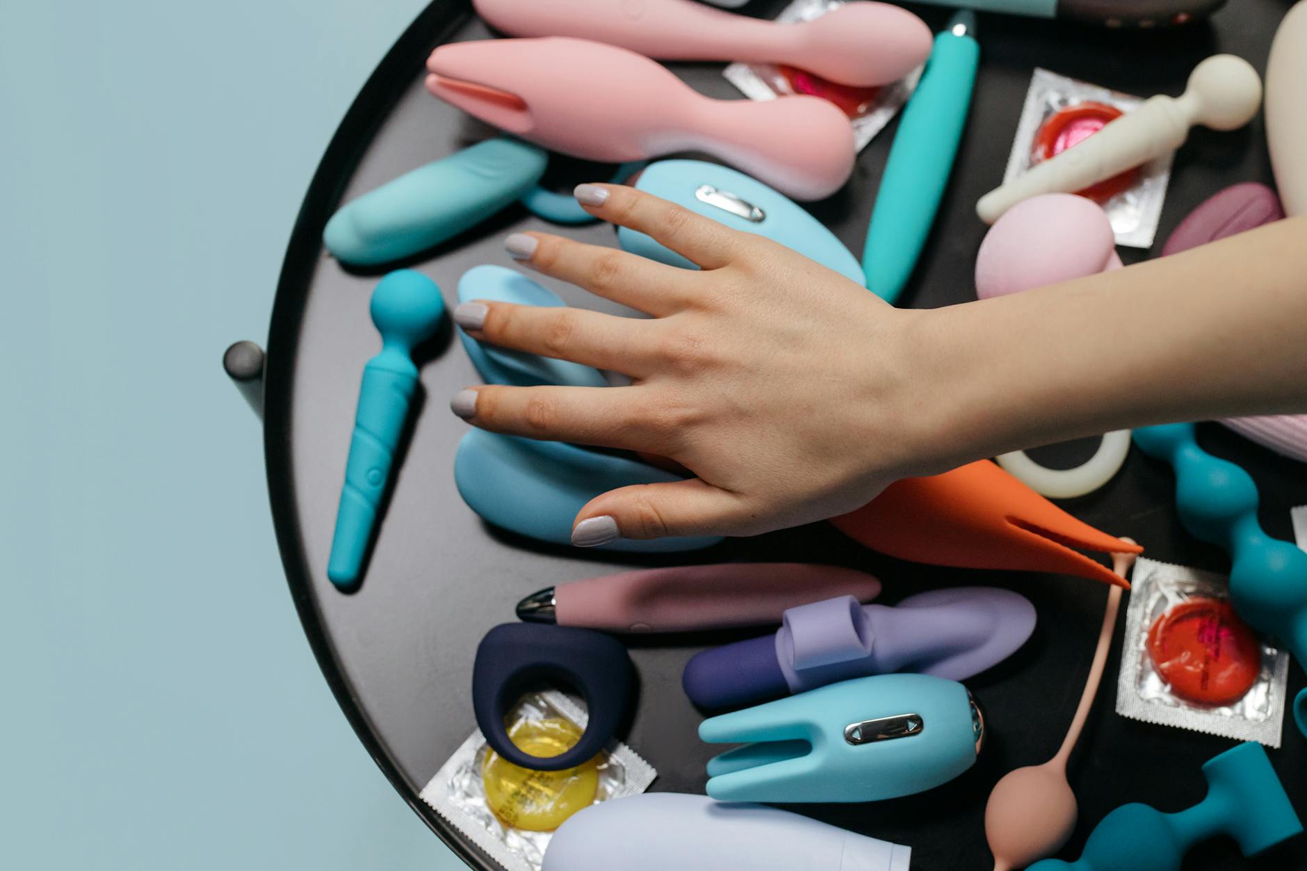 Deux mains tenant des vibromasseurs roses et bleus contre un fond pastel