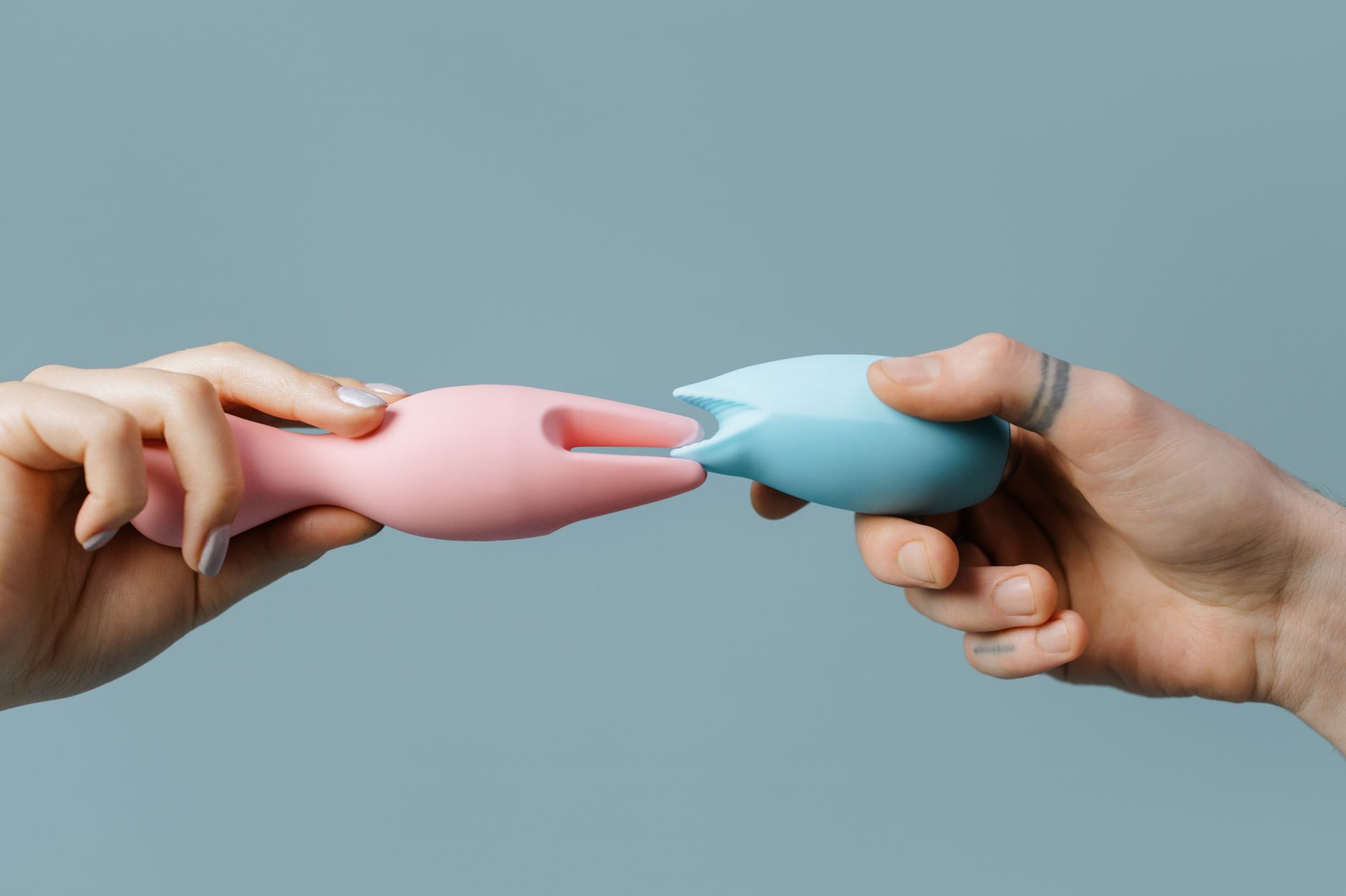 Deux mains tenant des vibromasseurs silicone rose et bleu sur fond pastel