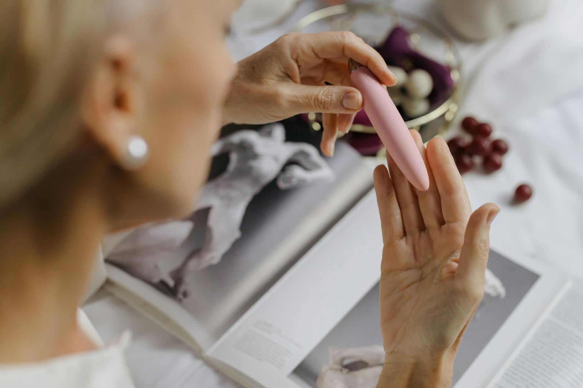 A woman holding a pink vibrator surrounded by books, representing a personal and intimate journey of healing and reclaiming pleasure.