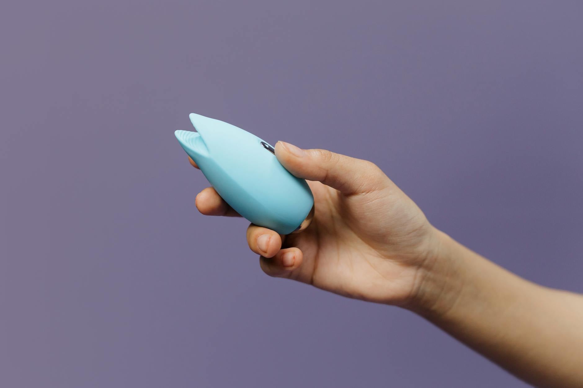 Un vibromasseur clitoral bleu tenu en main contre un fond violet, célébrant l'autonomisation sexuelle.