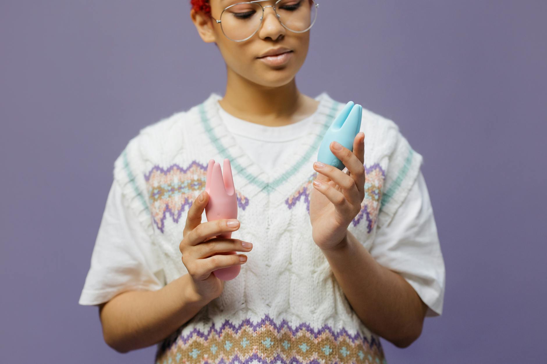 Woman holding blue and pink clitoral vibrators, exploring options for sensitive tissue pleasure.